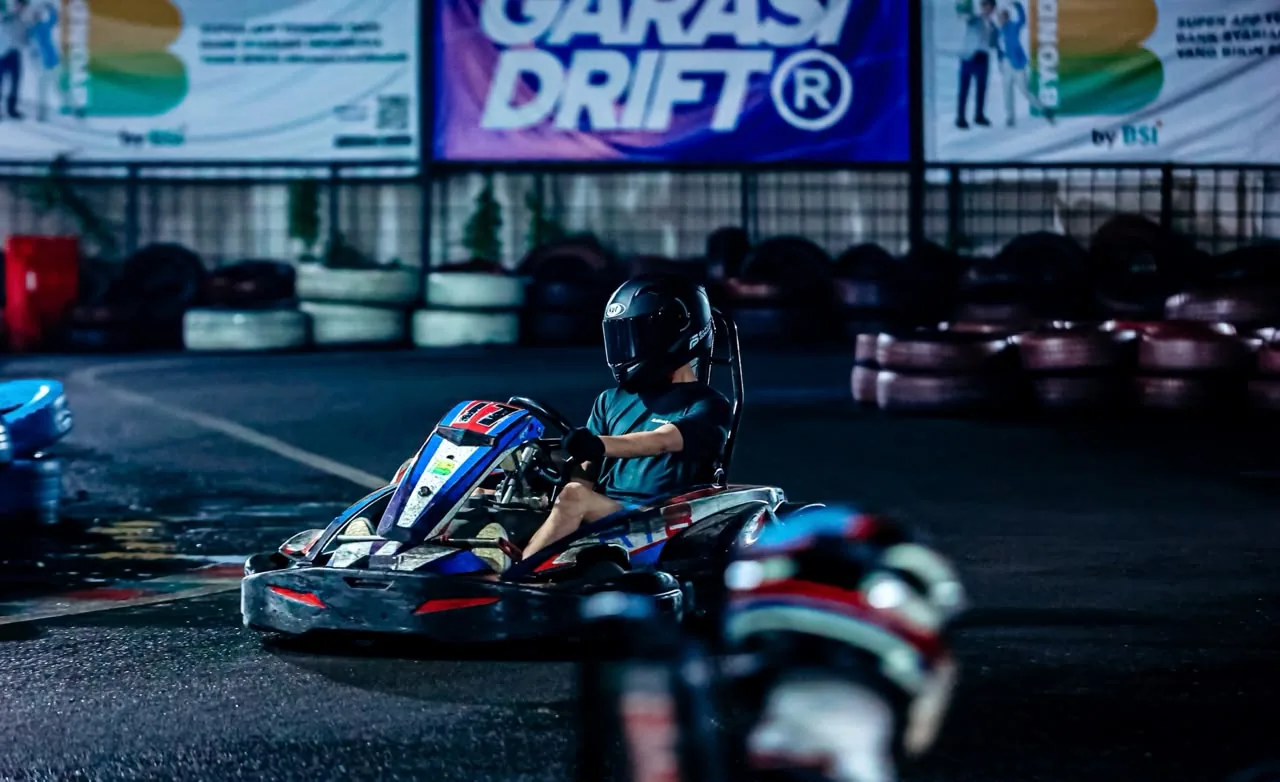 Driver in black helmet on track with Garasi Drift banner in the background